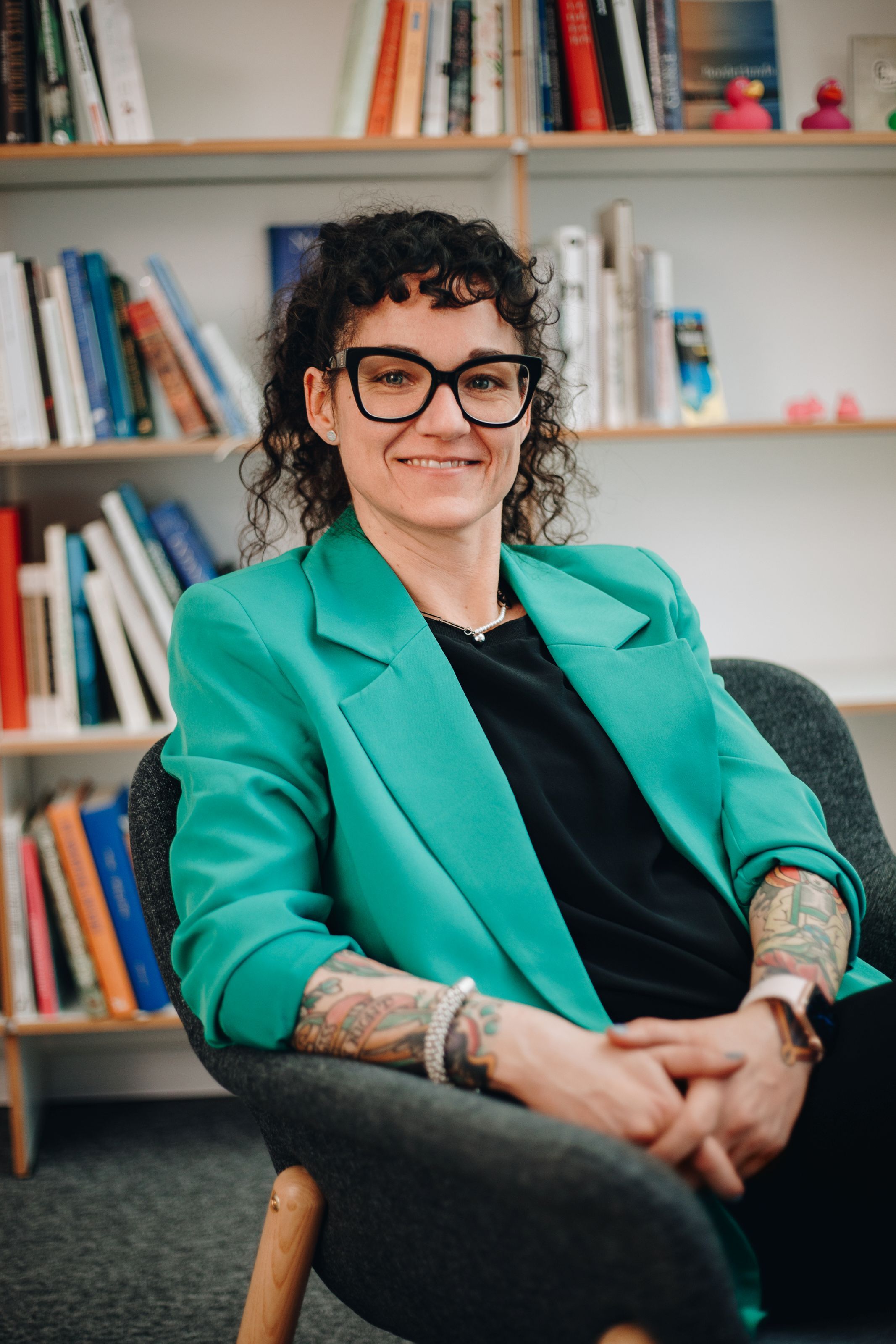 Susanne sitzt auf einem Stuhl vor einem Bücherregal.