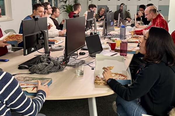 Teilnehmende vom Hackathon sitzen zusammen an einem Konferenztisch und essen Pizza