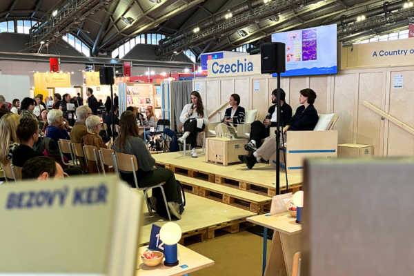 In between two book-covers, we see four people sitting on a stage and having a talk.