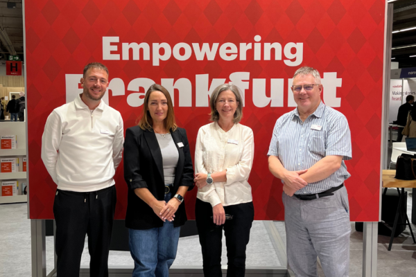 Four MVB-colleagues in front of a red banner of the mvb-stand on Frankfurt Book Fair.