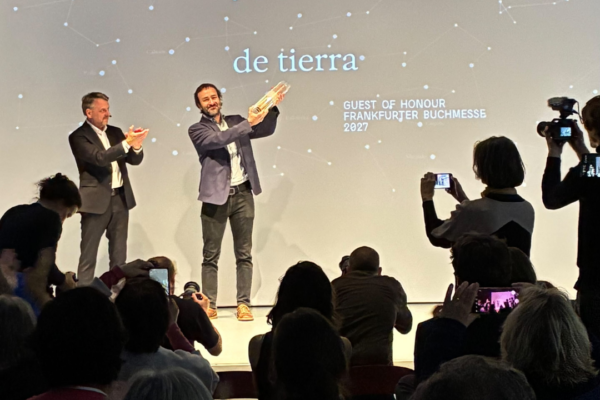 Two men on a stage who indicate at star constellations in the background.