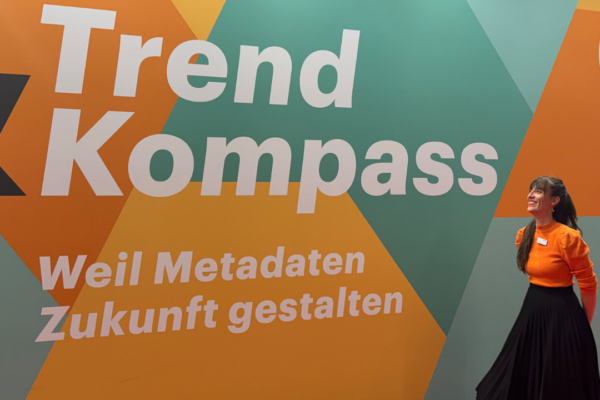 A woman stands in front of a huge MVB-metadata-poster in orange and turquoise.