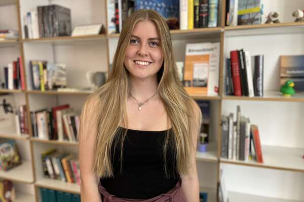 Olivia Zielke stands in front of a bookshelf and smiles.